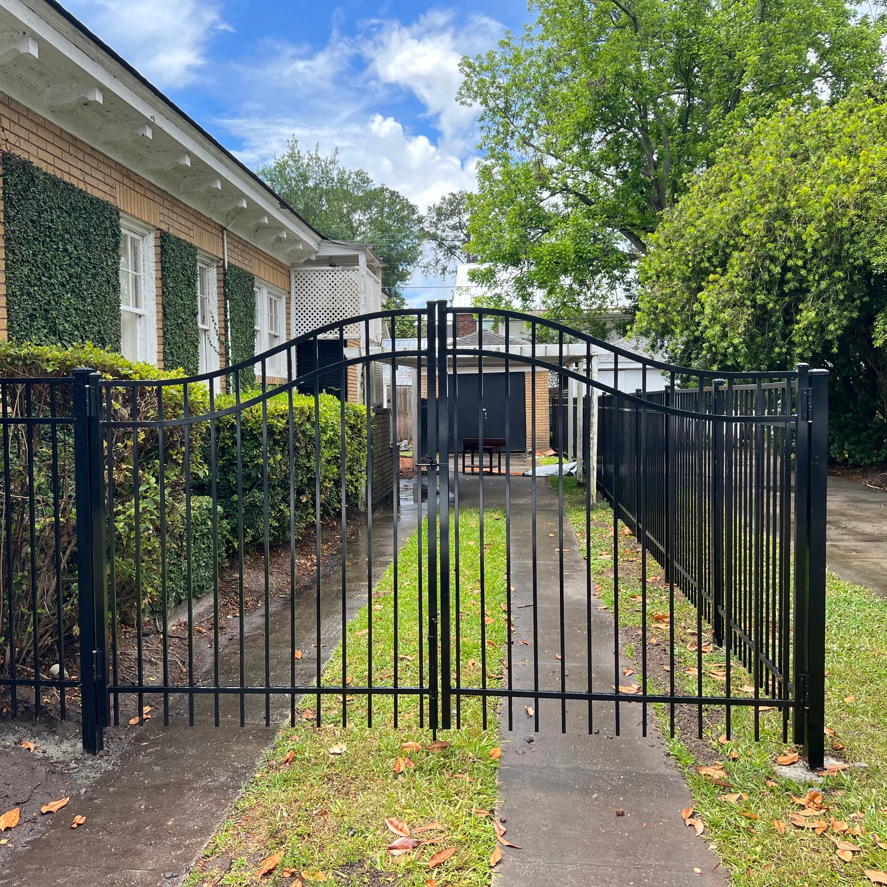 Black aluminum fence with an arched double gate in front of a brick home