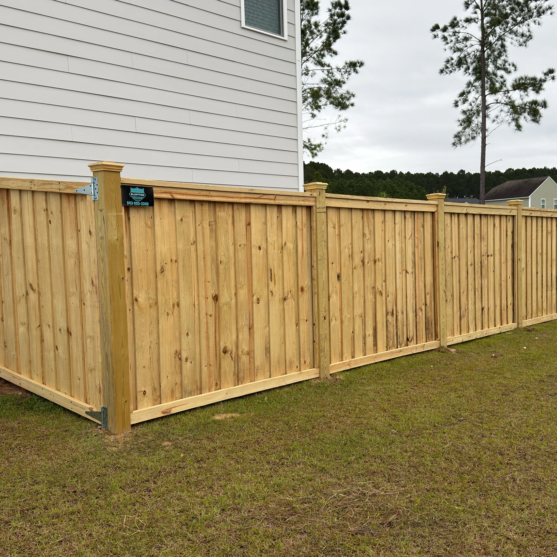 Capped wood privacy fence with a gate and a Bluffton Fence & Gutter sign
