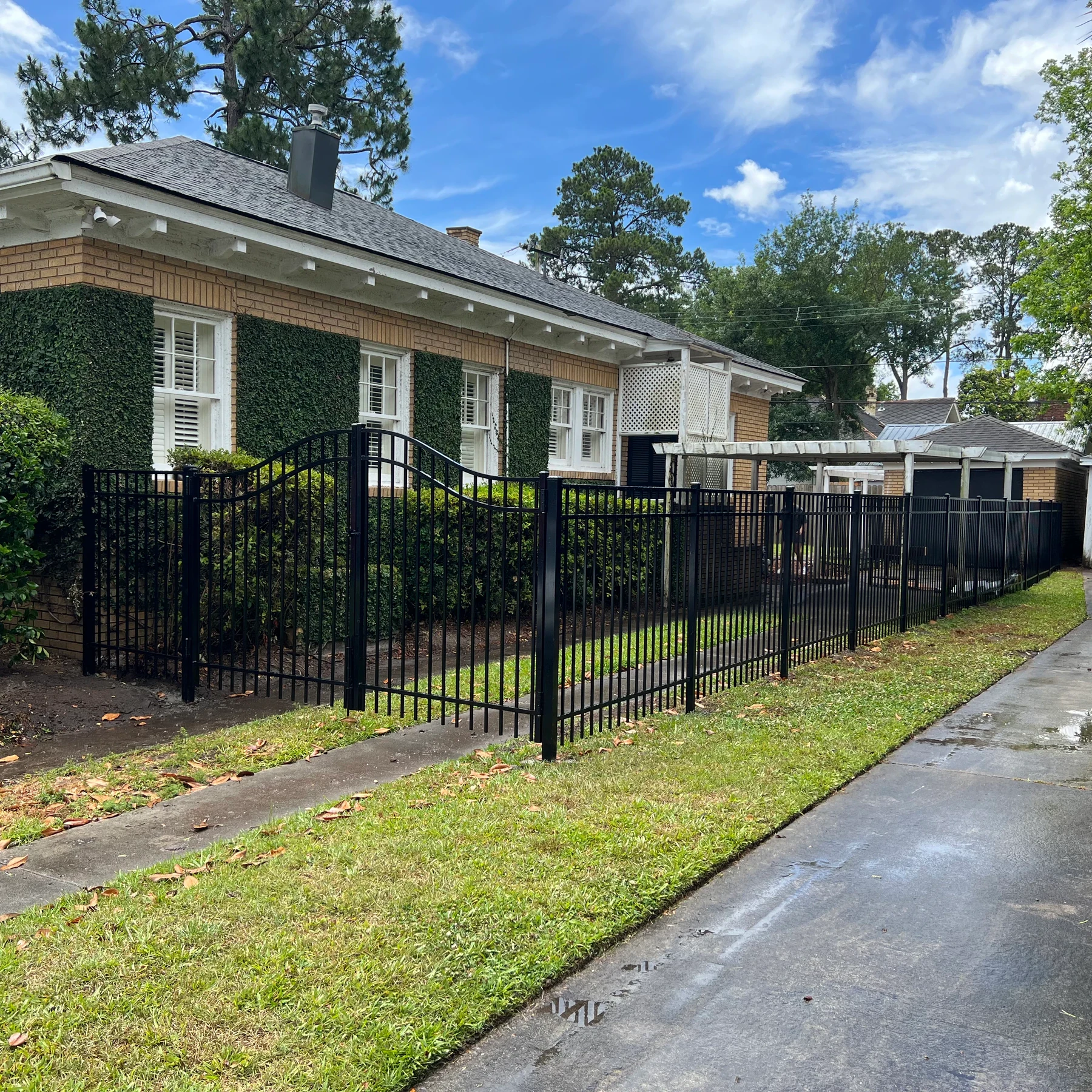 Black ornamental aluminum fence along a driveway beside a brick home