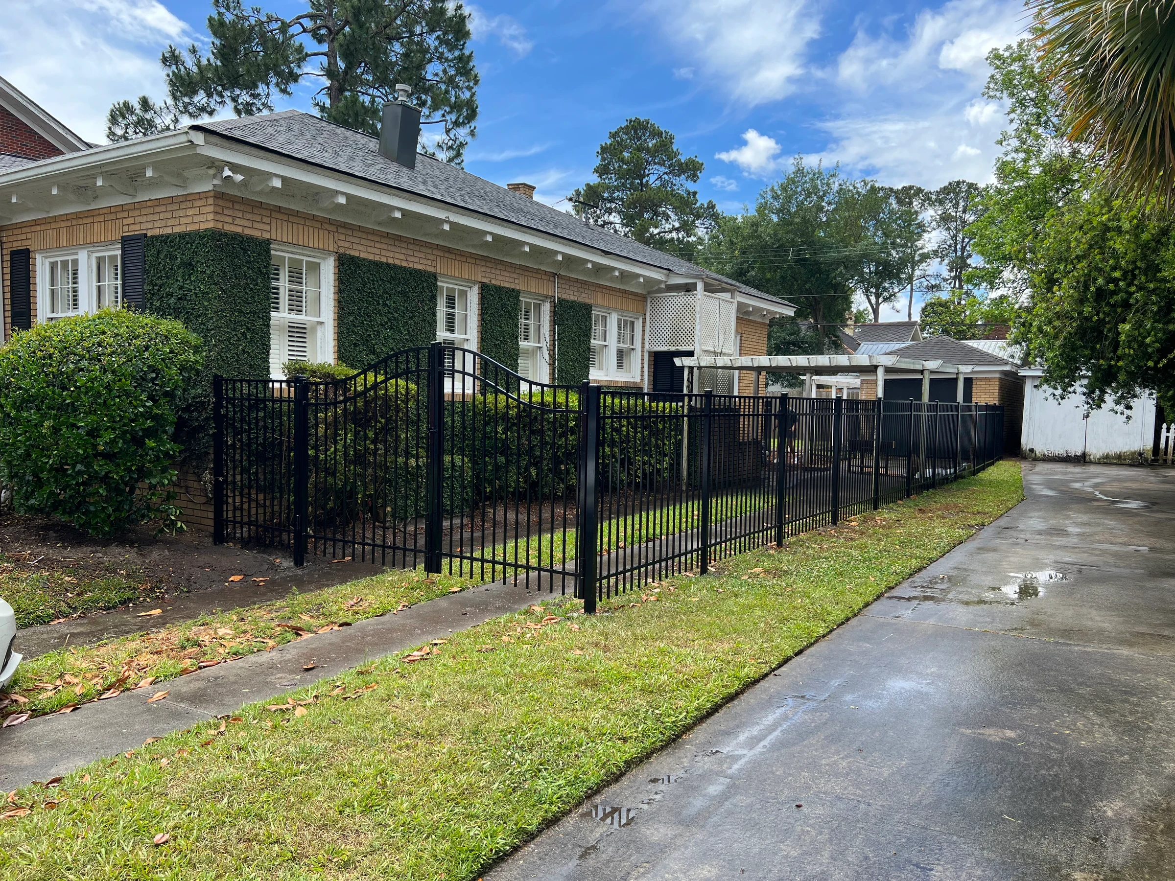 Black ornamental aluminum fence along a driveway beside a brick home
