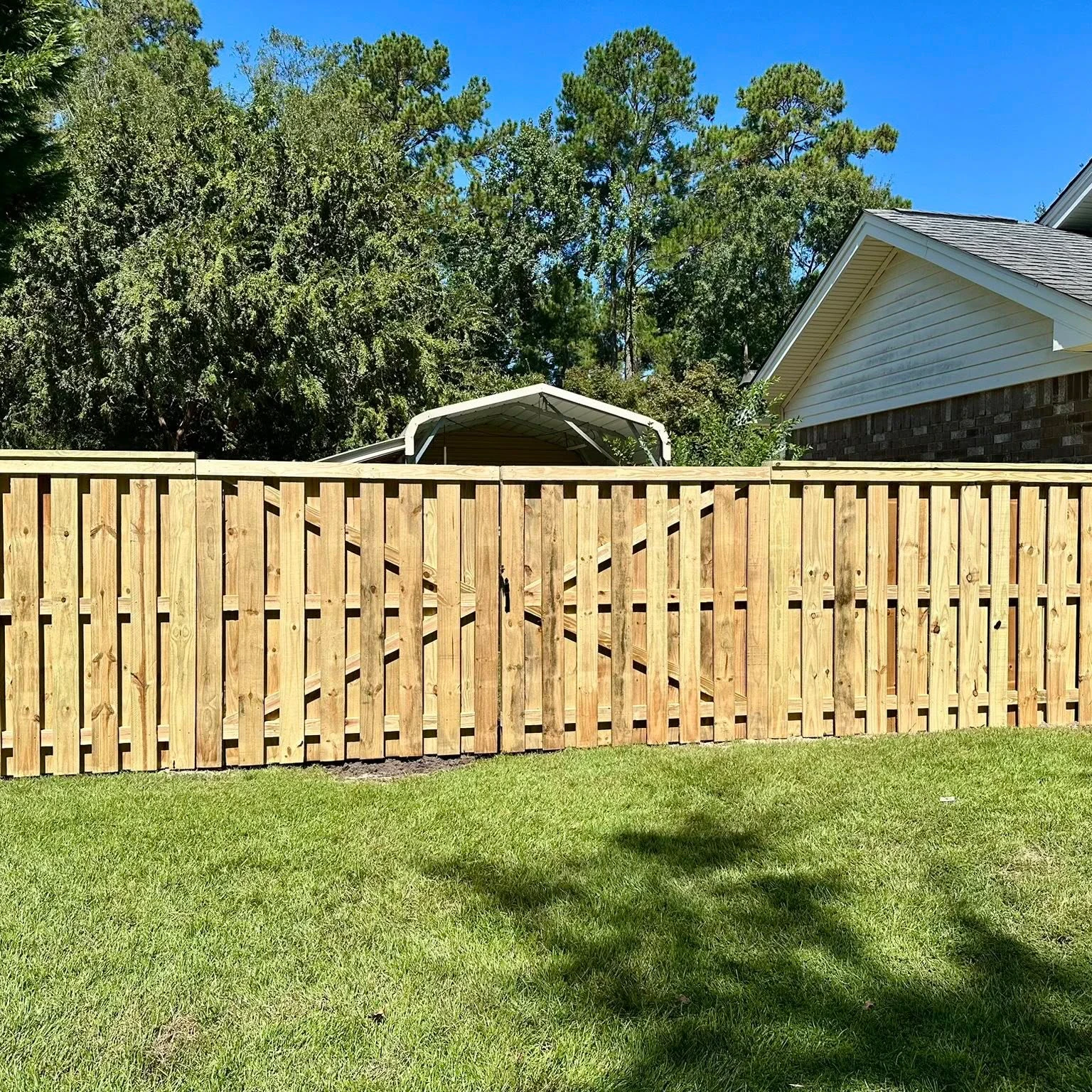 Wood shadowbox fence with a double drive gate beside a brick home