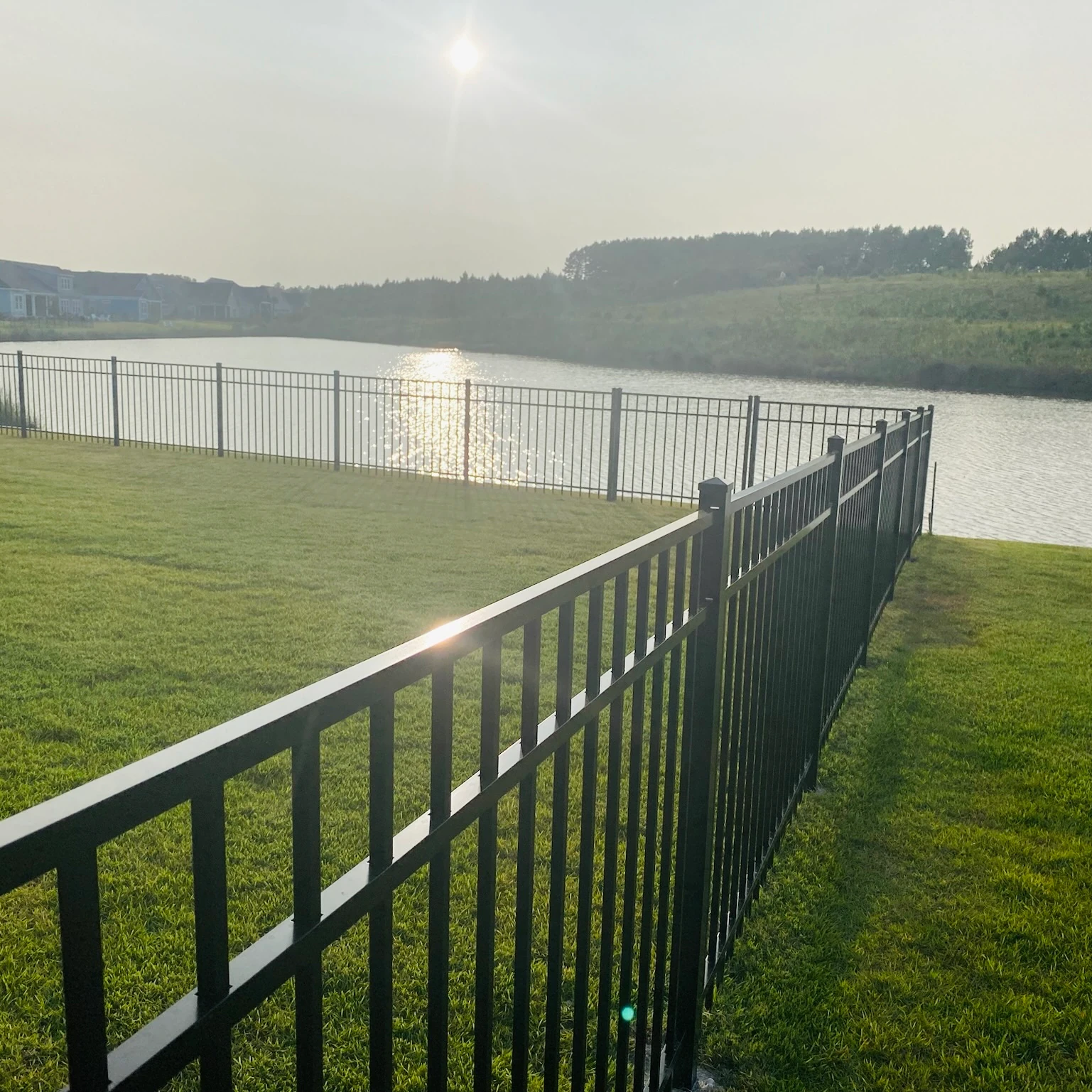 Black aluminum fence running along a pond at sunrise