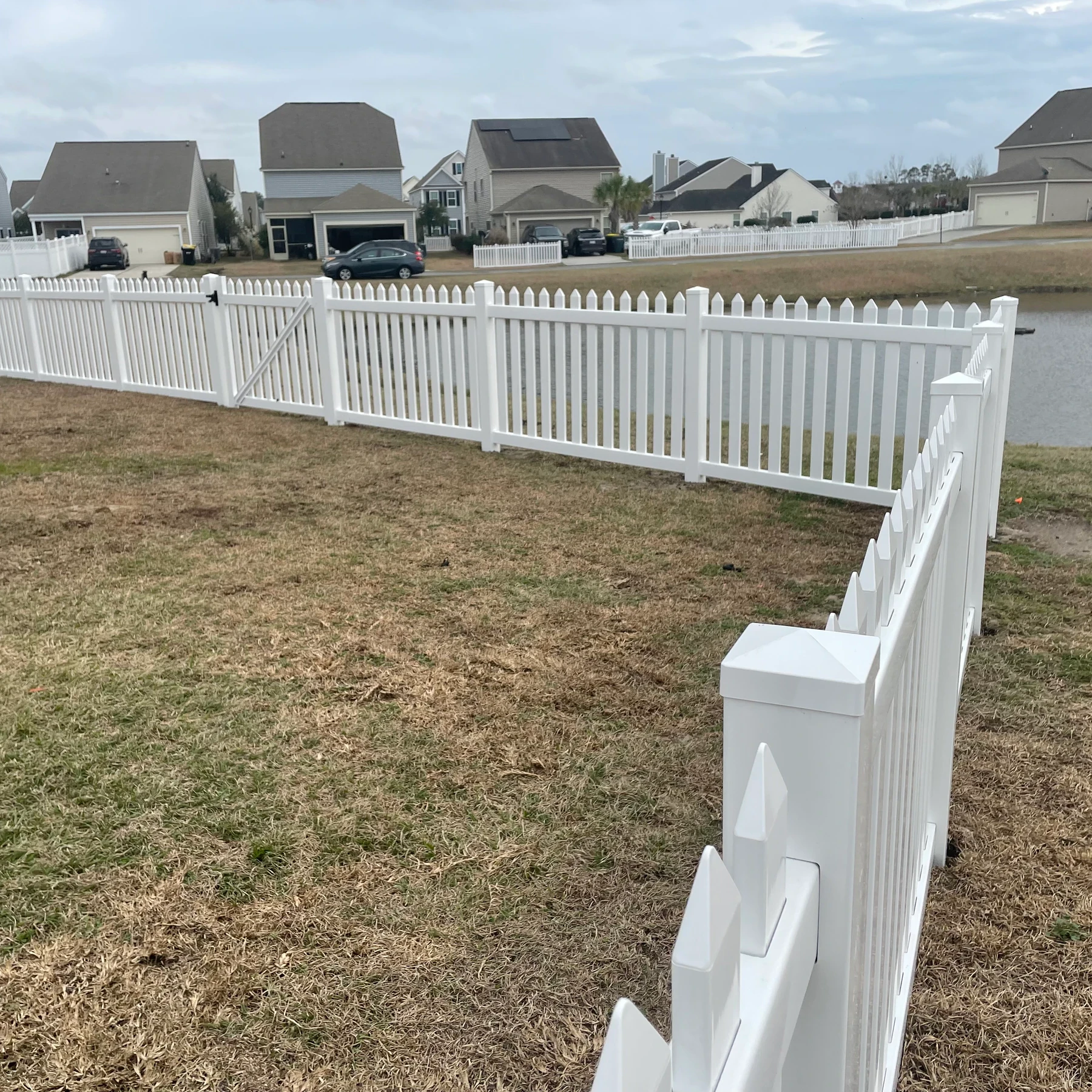 White vinyl picket fence along a pond in a residential neighborhood